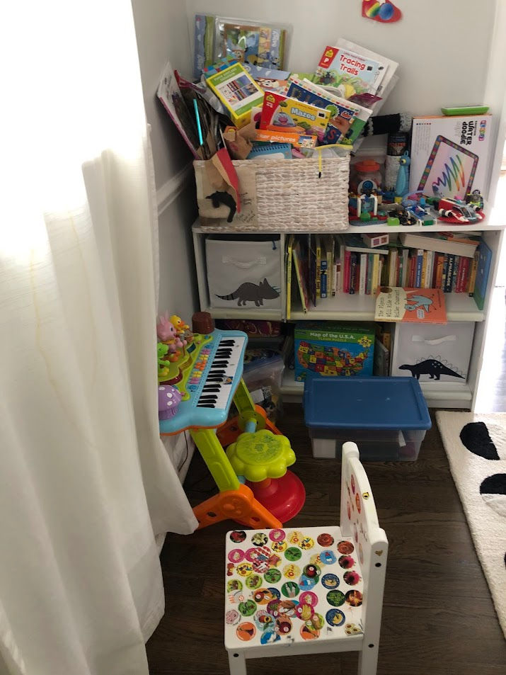kids' playroom, with a few toys on the ground in front of an overflowing bookshelf with an overflowing basket on top