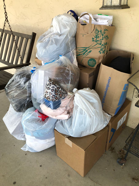 large pile of boxes, brown paper bags, and white garbage bags on a porch, filled with donations ready for porch pick up services