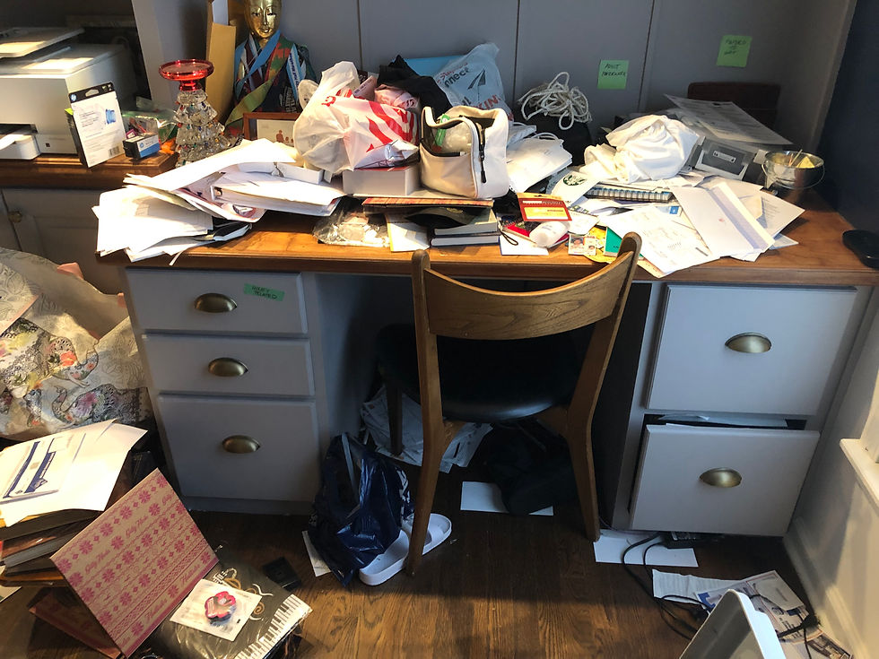 Cluttered desk with piles of paper and objects on it and surrounding it.