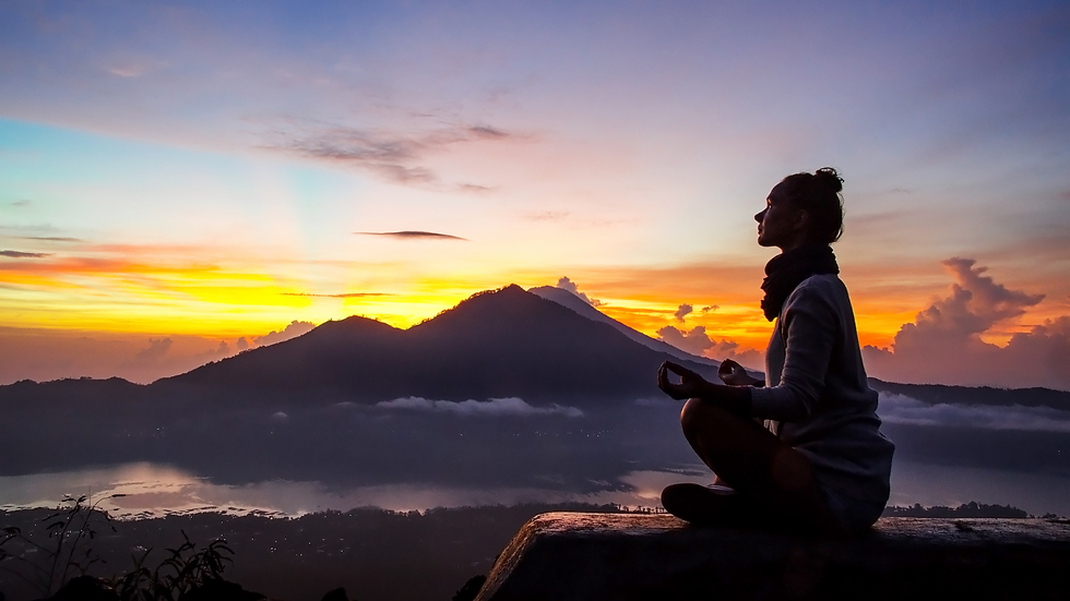 Mujer sentada meditando con las piernas cruzadas con un fondo de varias montañas al amanecer.