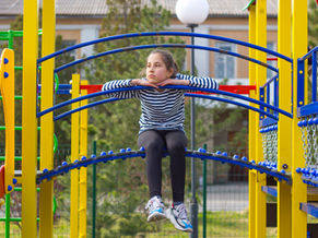A young kid somberly sits on playground equipment.