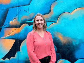 Dr. Watkins smiles in front of a multicolored mural in teal and orange.
