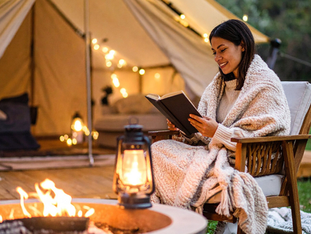 A woman relaxing with a book beside a safari tent and fire pit. This could be you at one of our Four Corners sites!