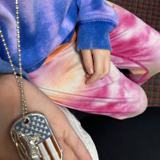 tie dye sweatshirt, tie dye pants, hand holding a medal with the US flag and a boat