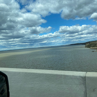 cloudy sky, dirty brown river, land to the top right, concrete barrier on bottom.