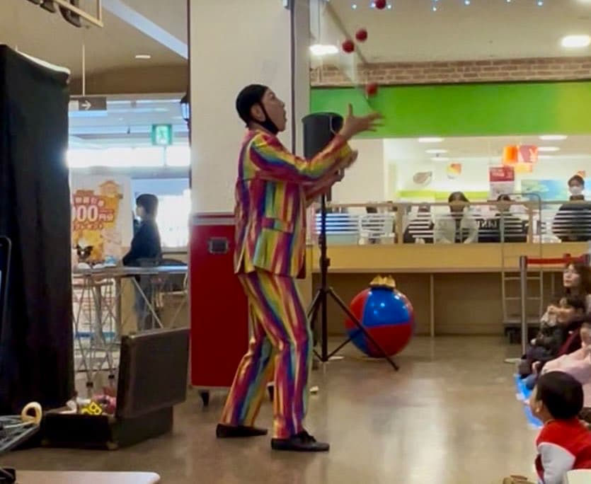 北海道のピエロTeTeが商業施設の新春イベントでカラフルな衣装を身にまとい、子どもたちの前でジャグリングパフォーマンスを披露している様子