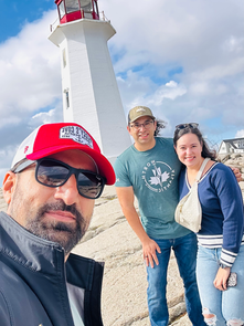 Safi Seaside Tours guide Asif day out with the tourist by the iconic Peggy's Cove red-and-white lighthouse, capturing a joyful moment on the rocky shore under a vibrant blue sky.