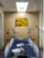 Hospital room bed with a wall behind it with a portrait of sunflowers