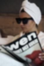A woman with a towel on her head and sunglasses reading a magazine