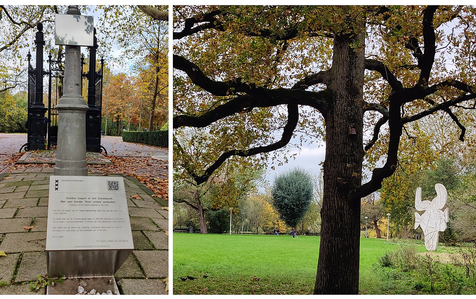 אנדרטה עם טקסט הולנדי על לוחית, שביל סלול, עצי סתיו. סצנת פארק עם עץ, דשא, אנשים רחוקים ופסל לבן .