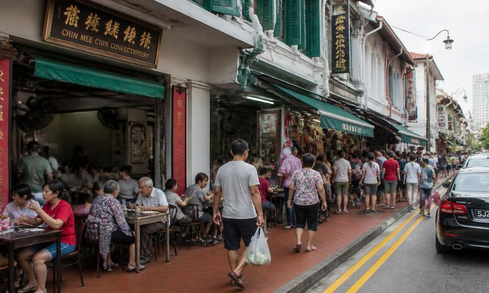 Crowded street outside a shophouse row, people dining on sidewalk tables under green awnings in a lively old-town scene