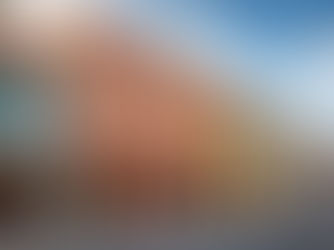 Colorful historic buildings with arches line a quiet street under a blue sky. People sit in cafes, creating a relaxed, vibrant atmosphere.