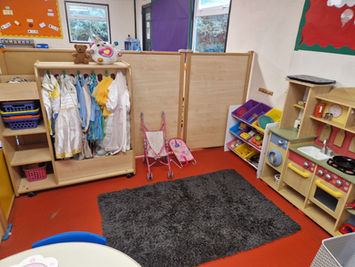 Children's play area with dress-up clothes, toy kitchen, and small rug.