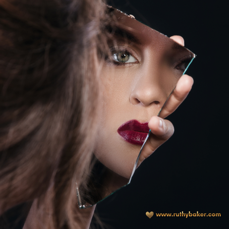 A woman looks into a fragment of a mirror at her reflection.