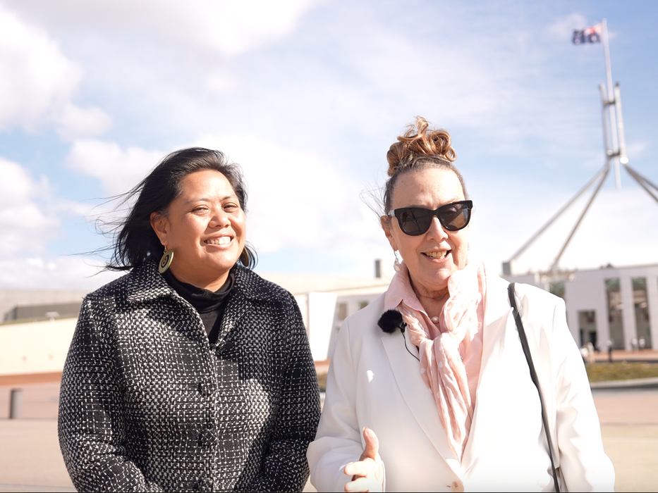 Two smiling women in front of Australian Parliament House