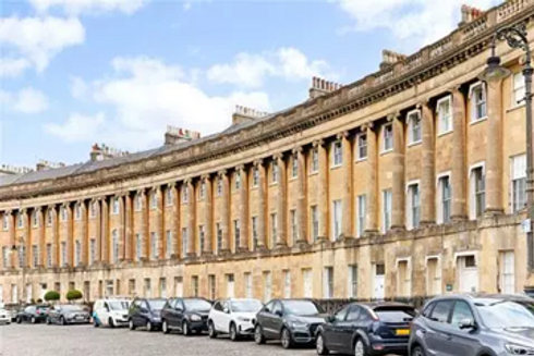 A row of cars parked in front of several buildings, showcasing urban architecture and street layout