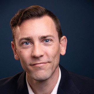 Executive headshot with 3-piece suit and tie on blue backdrop in studio.