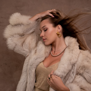 Glamour portrait of a young woman in fur with hair blowing in the wind photographed on custom backdrop in studio in Penn Valley, CA.