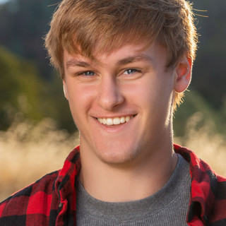 Senior Portrait of a young man in red plaid shirt with tall golden grass in the background photographed in Penn Valley, CA.