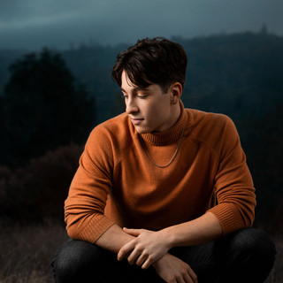 Dramatic High School Senior Portrait with orange turtleneck and white nikes with moody skies and artificial lighting.
