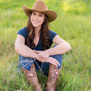 Outdoor photograph of a horse property realtor with cowboy hat and boots in tall green grass. Photographed in Rocklin, CA.