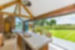 Rustic kitchen and dining area with wooden beams, concrete worktop, pendant lights, large windows and a view of an outdoor garden