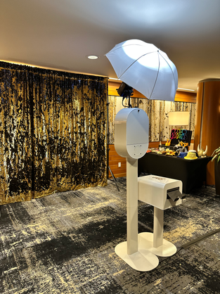 Photo booth kiosk with umbrella light and gold shimmer curtain backdrop at an upscale indoor event venue
