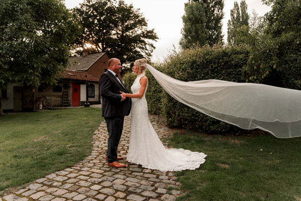 Foto van bruid met lange witte jurk en sleep, en bruidegom in kostuum