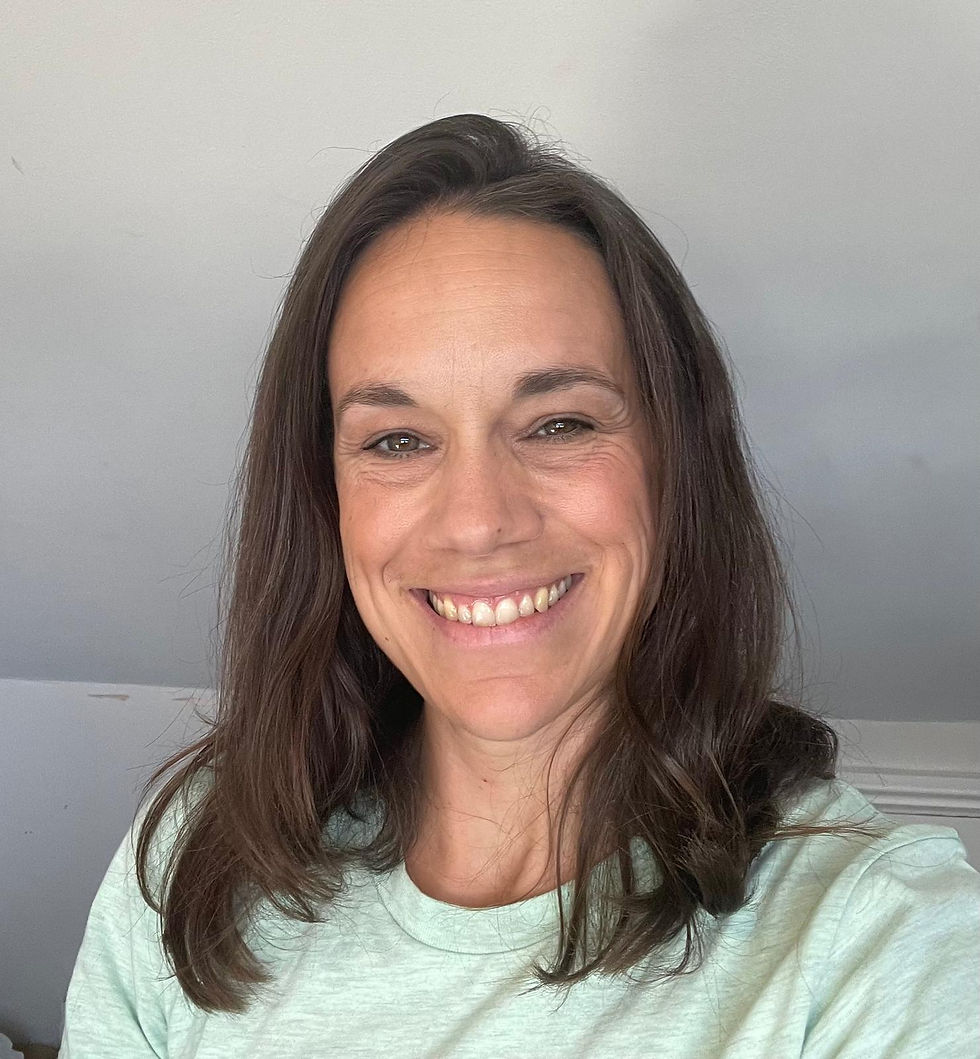 Woman with long brown wavy hair and brown eyes smiling at the camera wearing a light grey top.