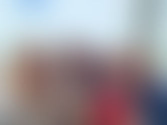 Four women stand close together smiling. Two have dark hair and two are blond. Behind them is a large windoe and a blue grey sky.