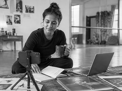 Performing artist planning digital content and creative communication strategy with notebook, phone camera, and laptop in a rehearsal studio