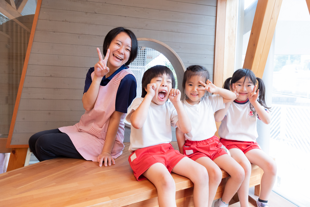 笑顔の保育士と子供たち、ピースサインをする、木製のベンチでポーズ。