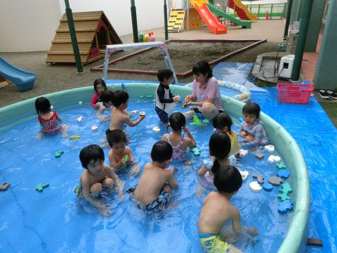 園児たちがプールで水遊び、先生と一緒に楽しんでいる様子です。楽しい夏の思い出