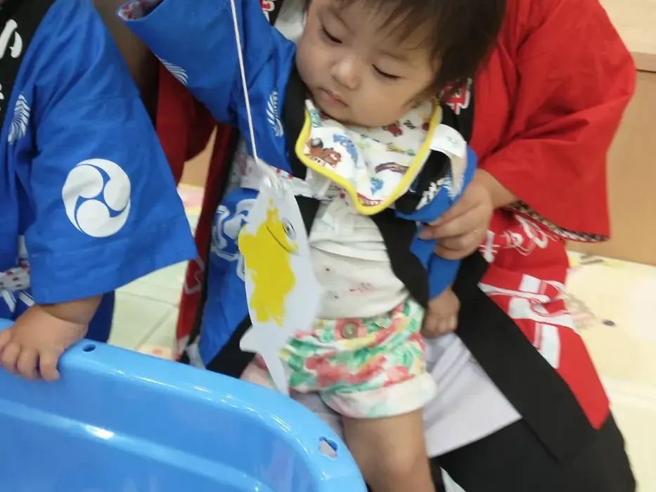 法被を着た子どもが青い桶で釣り遊びをする様子。