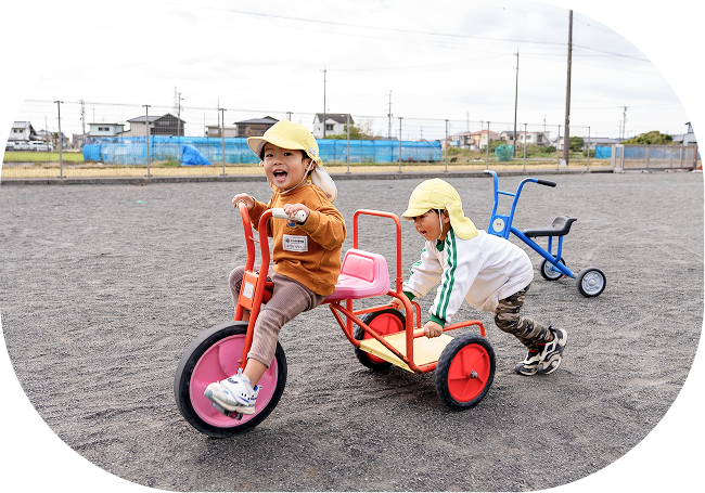 二人の子供が三輪車で遊んでいる様子です。楽しい遊びの時間、園の概要。