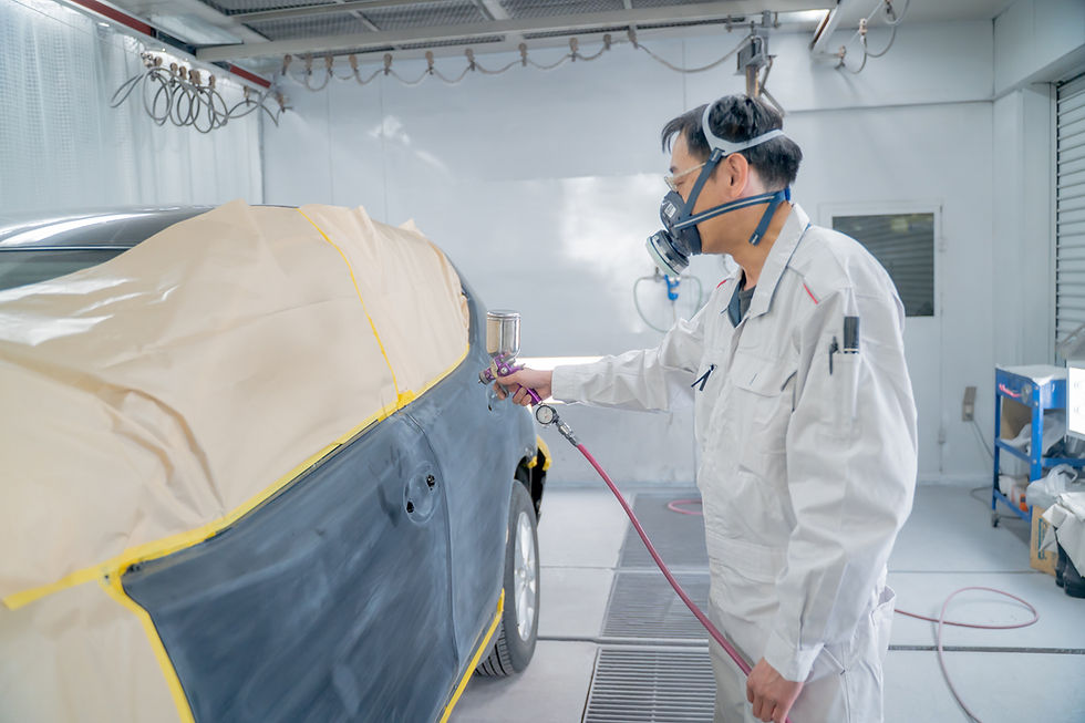 防護服とマスクを着用し、車にスプレー塗装を行う作業員