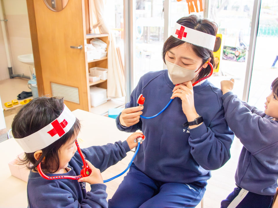 先生と子供たちが聴診器で医者ごっこをしている。