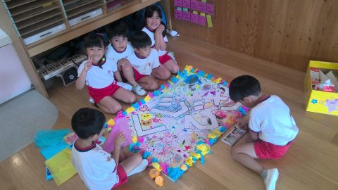 子供たちが楽しそうに遊ぶ様子。 2月【年少】お楽しみ会の様子。 描かれた絵を囲んで笑顔で集まる。