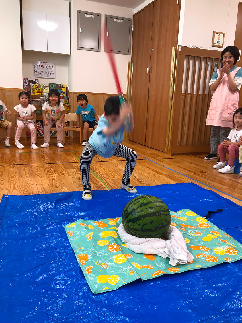 子供がスイカを割る様子。周りで見守る園児と先生。マジオブルームキッズ。