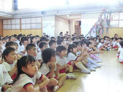 多くの子供たちが会場に座って見ている。５月のお誕生日会。多くの子供たちと先生たち。