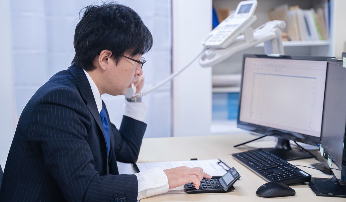 スーツを着た男性が電話をしながらPCと電卓で作業中