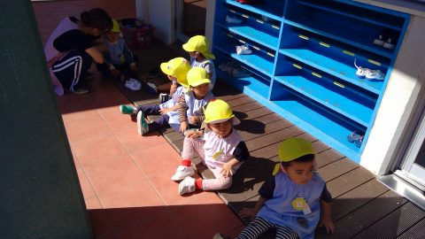 保育園の子供達が並んで座っている様子、黄色い帽子をかぶって、10月【年少々】今週の様子。