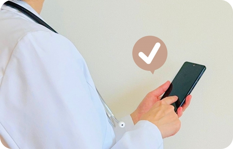 聴診器をかけた医師がスマートフォンを操作し、チェックマークで確認しています