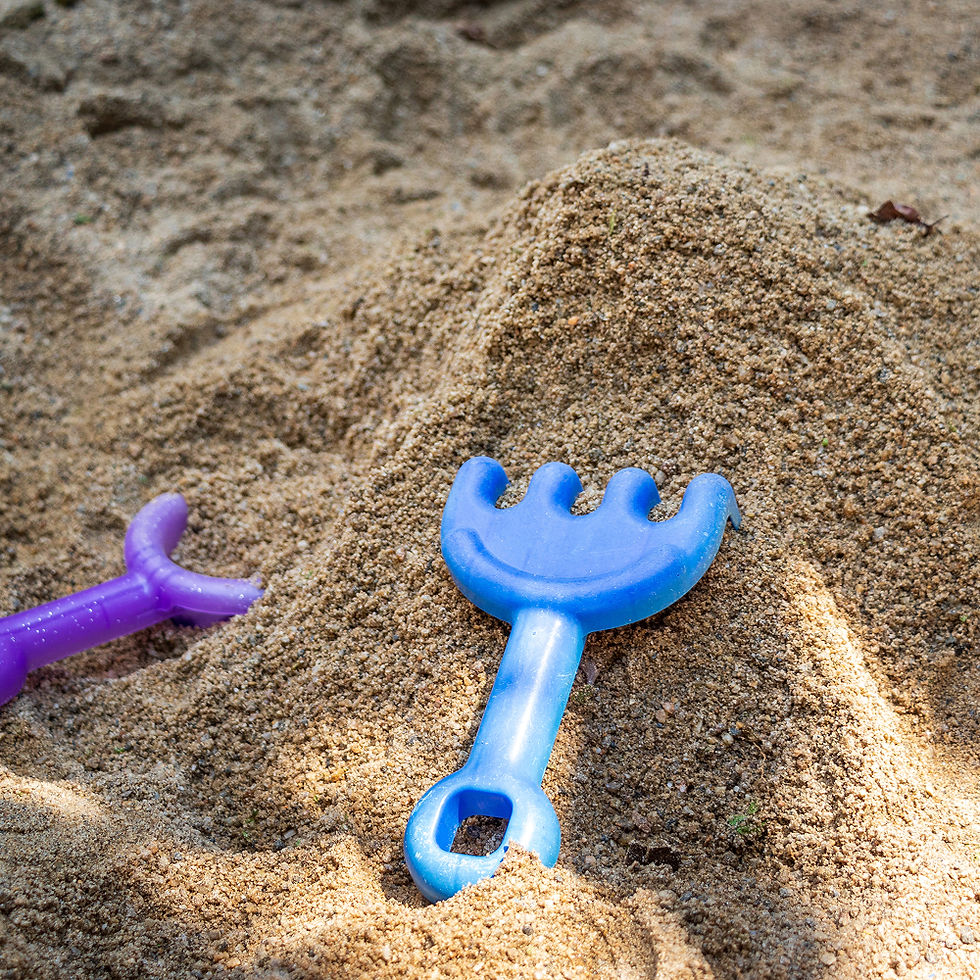 砂場で遊ぶ青い熊手と紫の熊手、背景に砂の山、子供のおもちゃ。