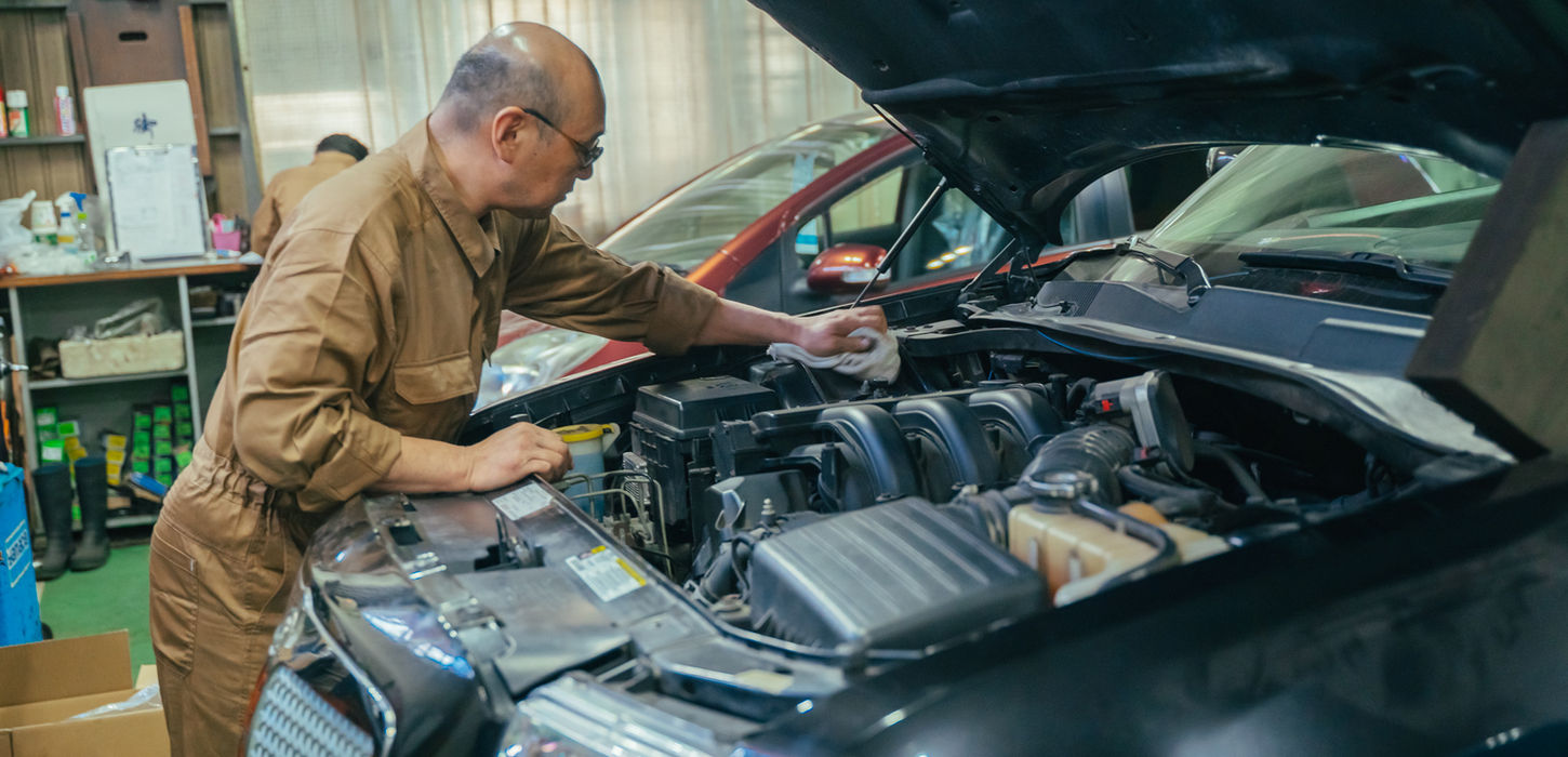 車のボンネットを開けてエンジンルームを点検する整備士