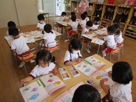 園児たちが絵を描く様子。カラフルな絵本とクレヨン。5月【年中】英語指導、集中している様子。