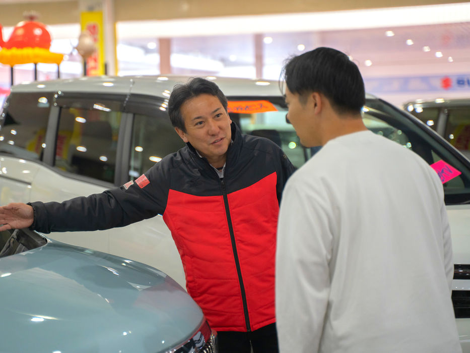 ショールームで車を指さしながらお客様に説明する男性スタッフ