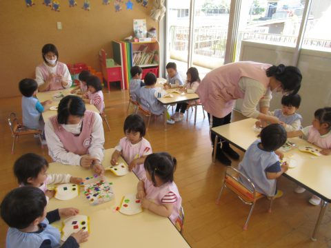 保育園の子供たちが製作活動中、先生と一緒に楽しそう。笑顔で製作に取り組む様子。