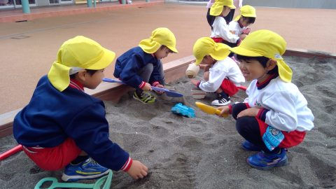 砂場で遊ぶ子供たち、黄色い帽子をかぶり、楽しそうに砂遊びをしています。
