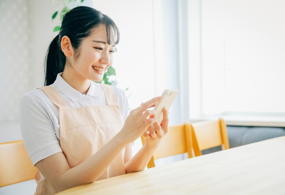 スマートフォンを操作して笑顔で過ごすエプロン姿の先生